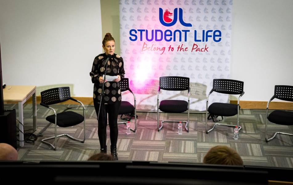 Woman presenting at a UL Student Life event with empty chairs on stage.